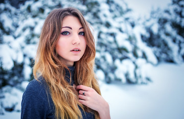 Pretty young girl posing in the winter in cold forest with pine