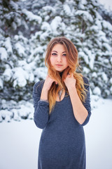 Pretty young girl posing in the winter in cold forest with pine