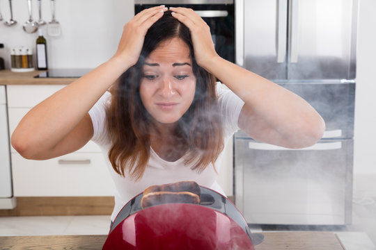 Frustrated Woman Looking At Burnt Toast In Toaster
