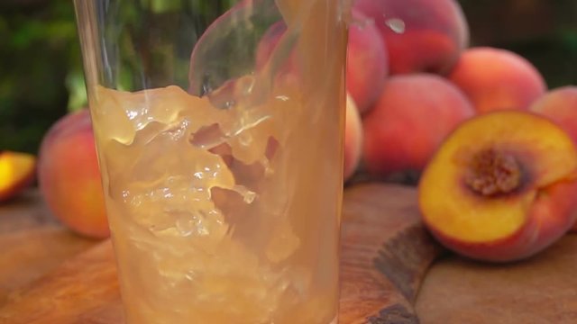 Peach juice is poured into a glass, background of peaches