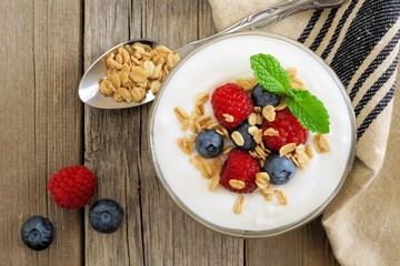 Greek yogurt with raspberries, blueberries and granola, overhead scene on rustic wood
