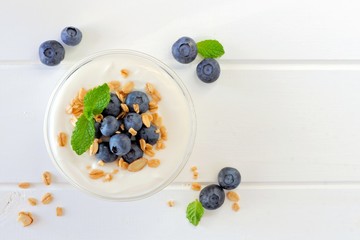 Greek yogurt with blueberries and granola, above view on white wood