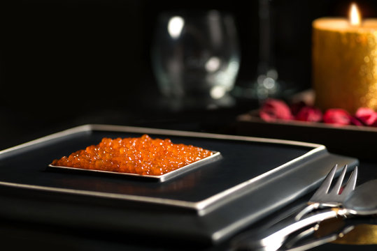 red caviar lies on a square ceramic stylish black plate