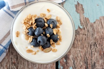 Bowl of yogurt with blueberries and granola, close up over a wooden background