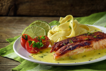 Grilled salmon dish with saffron sauce and tagliatelle pasta on dark rustic wood