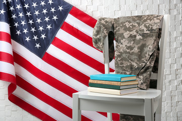 Chair, books, soldier uniform and USA flag near light textured wall. Military education concept