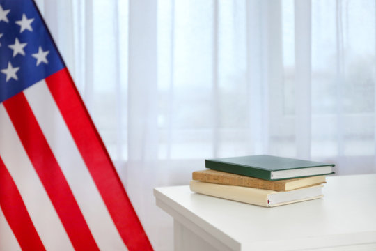 Books on white table and blurred USA flag near window. Education concept