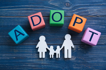 Cubes with word ADOPT and figure in shape of family on color wooden background