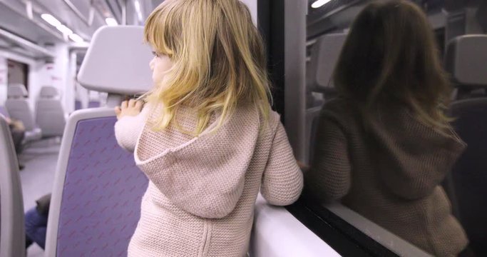 4k video. Three years old blonde child sitting backwards looking through window in a train inside a tunnel or by night
