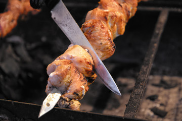 Street food. Salesman tries if chicken meat roasted on skewer is ready. Food stall on Christmas fair in Ukraine