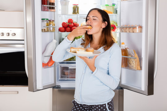 Woman Eating Sweet Food Near Refrigerator