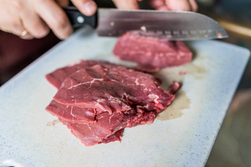 Hands with large knife cutting beef meat into strips
