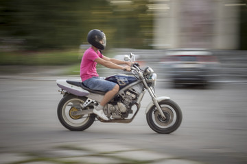 Fototapeta na wymiar Man riding motorcycle. Young guy in a pink T-shirt and denim shorts, with a motorcycle helmet on his head quickly rides on a motorcycle on the street