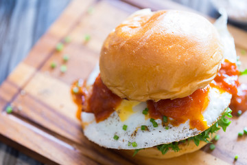 Hamburger, cheese and fried egg is placed on a wooden serving dish.
