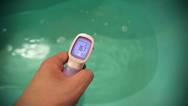 Measuring water temperature in baby bath tub before bathing with infrared pyrometer - contactless thermometer.