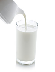 Milk pouring from a jug into a glass on white background