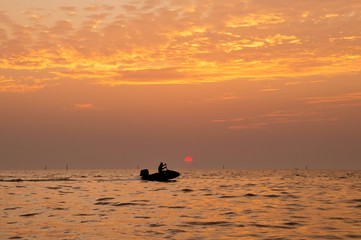 Silhouette of man driving jetski on the sea with during sunset
