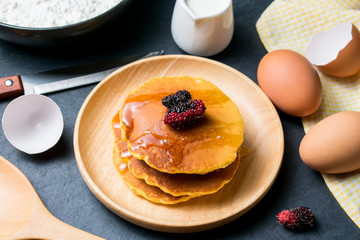 Pancakes with fresh mulberry and honey on black stone background