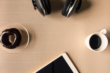 Top view of headphones with tablet, coffee cup and donut on table