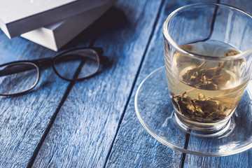 Cup of tea with book and glasses on wooden table