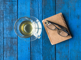 Top view of tea cup with notebook and glasses on blue wooden table