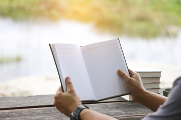 Stock Photo:.Man reading a book and writing notes on wooden tabl