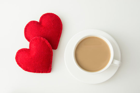 Valentine's day card. White mug of hot coffee with milk and red felt heart. Top view.