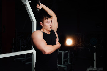 Fototapeta na wymiar Portrait of a muscular young man lifting weights on gym background.