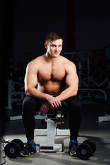 Fototapeta na wymiar professional bodybuilder sitting on the bench, resting between exercises with dumbbells at gym. Big