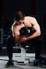 Fototapeta na wymiar professional bodybuilder do exercises for biceps sitting on the bench, with dumbbells at gym. Big
