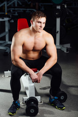 Fototapeta na wymiar professional bodybuilder sitting on the bench, resting between exercises with dumbbells at gym. Big