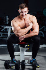 Fototapeta na wymiar professional fitness bodybuilder sitting on the bench and demonstrates muscles of your body after a workout, at gym.