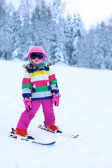 Naklejka premium Happy child enjoying vacation in Alpine resort in Austria. Little girl skiing in mountains. Active sportive toddler learning to ski. Winter sport for family. Skier racing in snow.