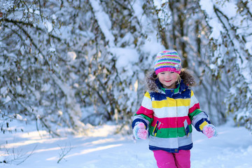 Fototapeta na wymiar Portrait of beautiful toddler girl playing outdoors with snow. Happy little child wearing colorful knitted hat and blue coat enjoying winter day in the park or forest.