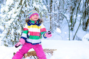 Fototapeta na wymiar Portrait of beautiful toddler girl playing outdoors with snow. Happy little child wearing colorful knitted hat and blue coat enjoying winter day in the park or forest.