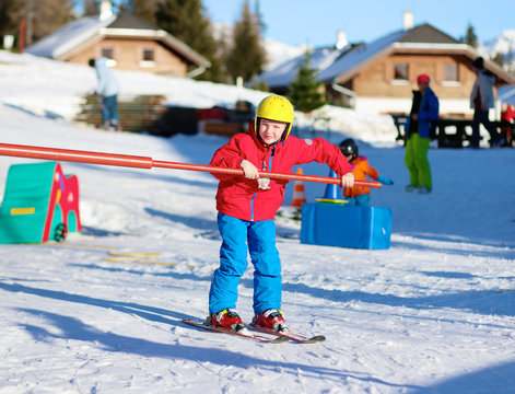 Happy school boy in colourful snowsuit learning to ski in alpine resort on sunny day during winter vacation