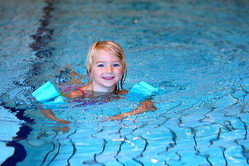 Happy preschooler girl learning to swim in community swimming pool. Little swimmer enjoying group lesson at sport school.