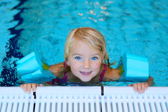 Happy Preschooler Girl Learning To Swim In Community Swimming Pool. Little Swimmer Enjoying Group Lesson At Sport School.