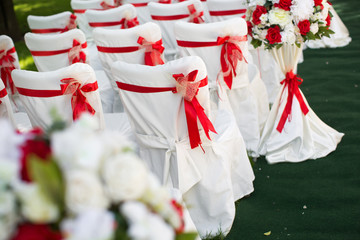 Wedding ceremony outdoors. White chairs with red ribbon.