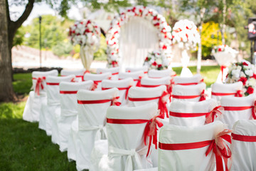 Wedding ceremony outdoors. White chairs with red ribbon.