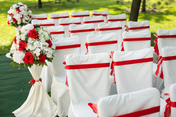 Wedding ceremony outdoors. White chairs with red ribbon.