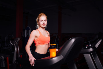 Fototapeta na wymiar Young beautiful cute girl in fitness model in the gym running on the treadmill with bottle
