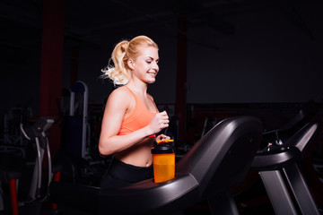 Obraz na płótnie Canvas Young beautiful cute girl in fitness model in the gym running on the treadmill with bottle
