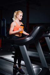 Naklejka na ściany i meble Young beautiful cute girl in fitness model in the gym running on the treadmill with bottle