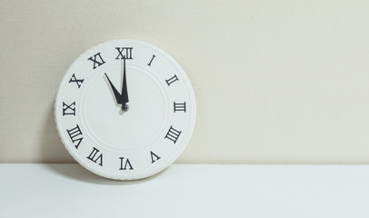 Closeup white clock for decorate show 11 o'clock on white wood desk and cream wallpaper textured...