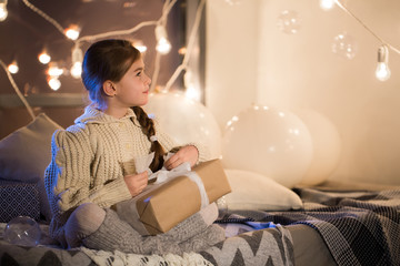 Naklejka premium Beautiful little girl sitting on bed with a gift in its hands.
