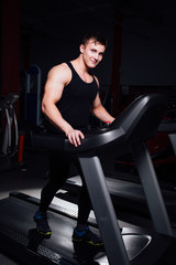 Young strong big man fitness model in the gym running on the treadmill with water bottle.