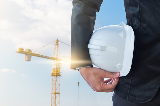 The business man holding the helmet with crane background
