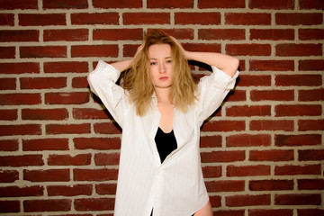 Молодая девушка стоит в белой рубашке и черном боди возле кирпичной стены, студийная съемка