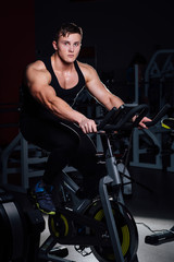 Portrait of a handsome man workout on  fitness  the exercise bike   dark at gym.